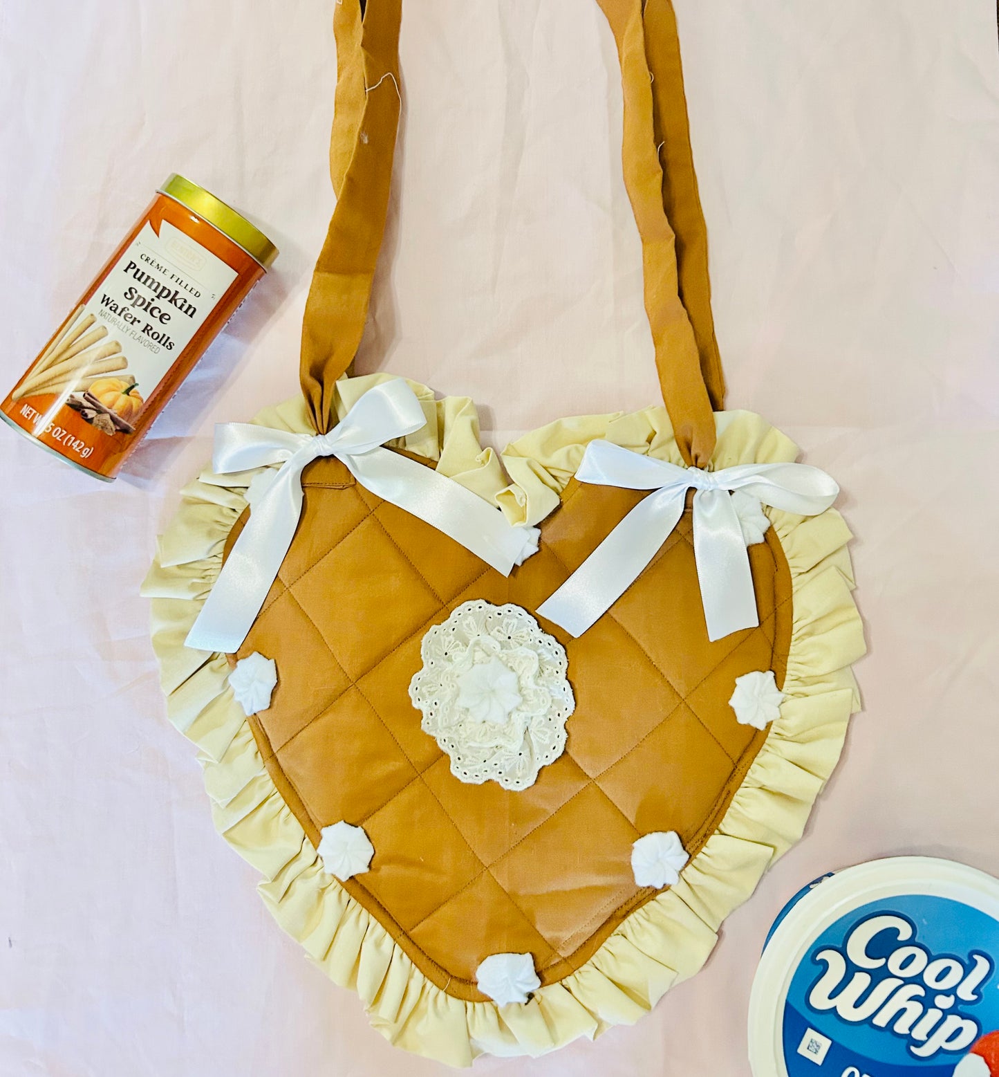 Heart-shaped quilted bag with ruffles and a bow, surrounded by pumpkin spice latte and Cool Whip containers on a light pink background.