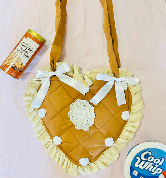 Heart-shaped quilted bag with ruffles and a bow, surrounded by pumpkin spice latte and Cool Whip containers on a light pink background.